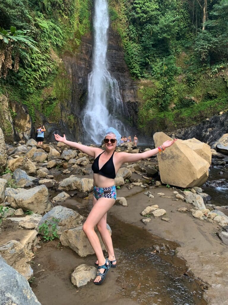A girl in a shower cap standing in front of a Bali waterfall after ear surgery in Vietnam