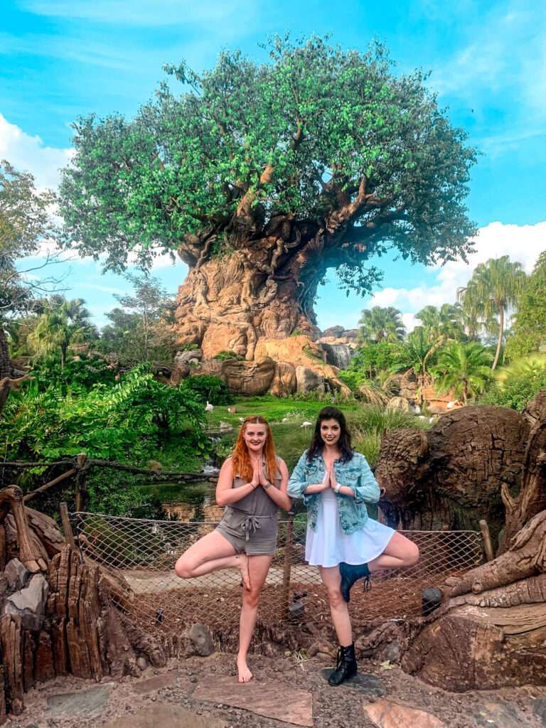 Two friends doing tree yoga pose in front of the tree at Animal Kingdom Disney, Florida
