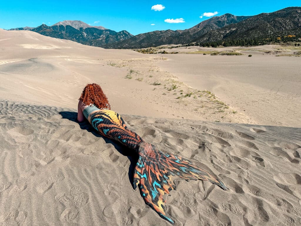 A mermaid laying face down in the sand in the mountains