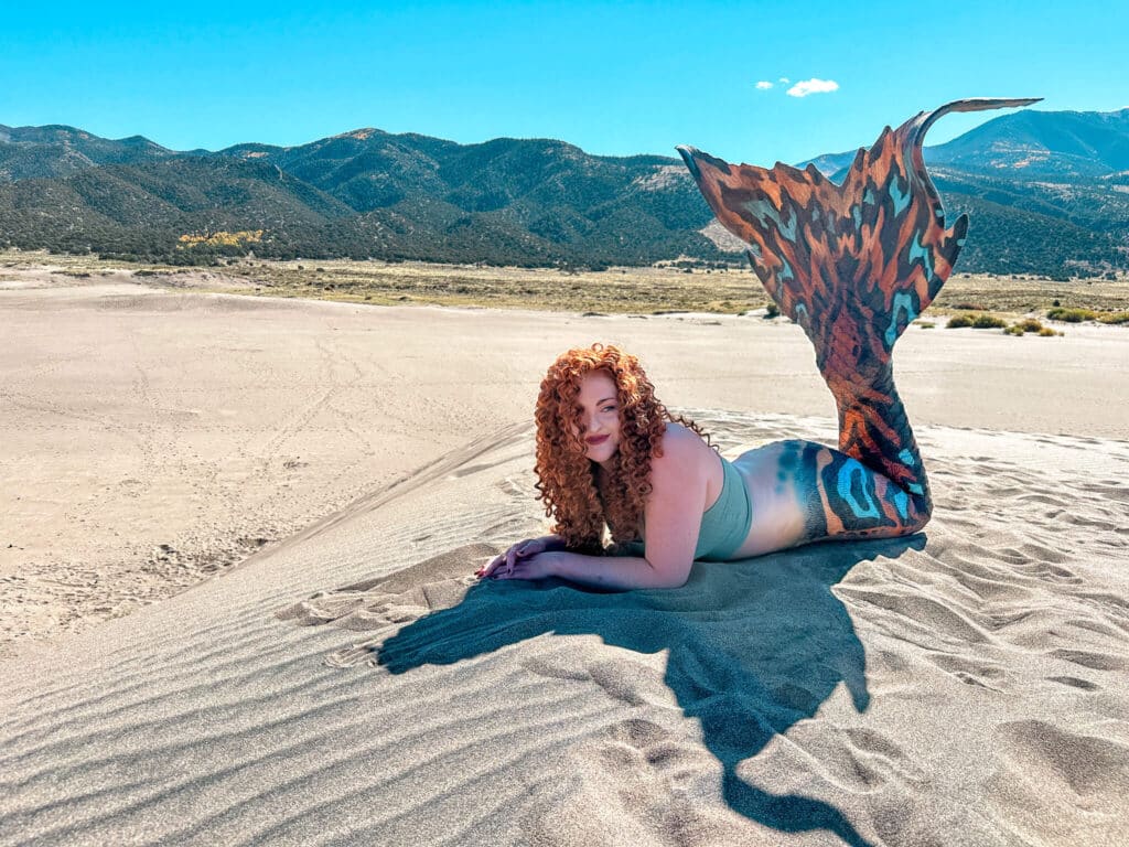 A mermaid on the Great Sand Dunes with the mountains in the foreground.