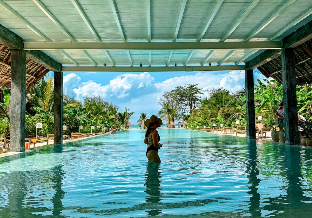 Girl in swimsuit looking over a pool at a beach resort in Zanzibar