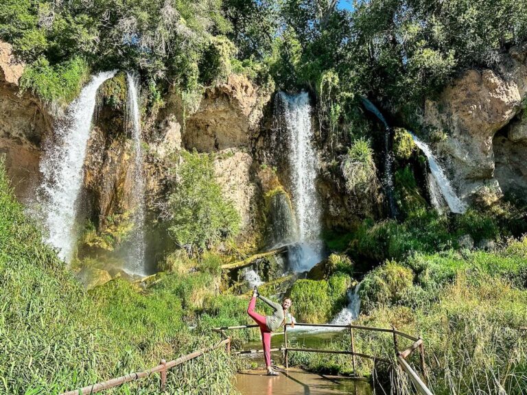 A yoga teacher doing "dancers pose" in front of three tall waterfalls in Colorado