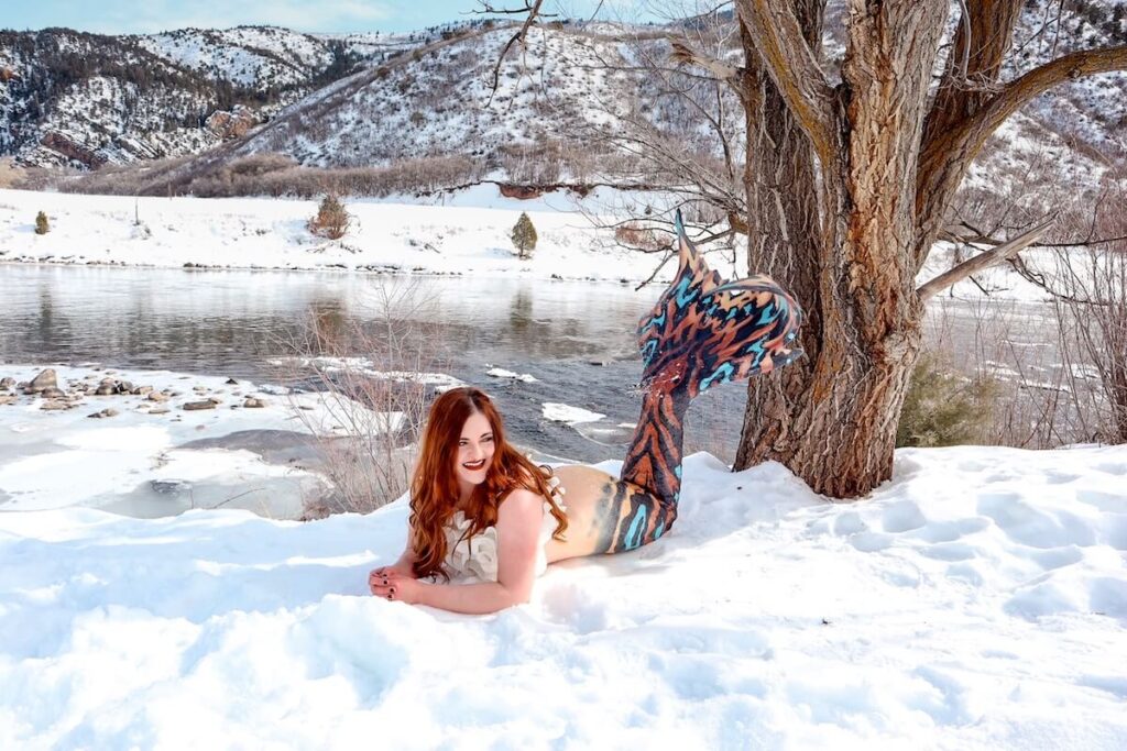 The Bucket List Mermaid posing in the snow with a river and mountains in the background