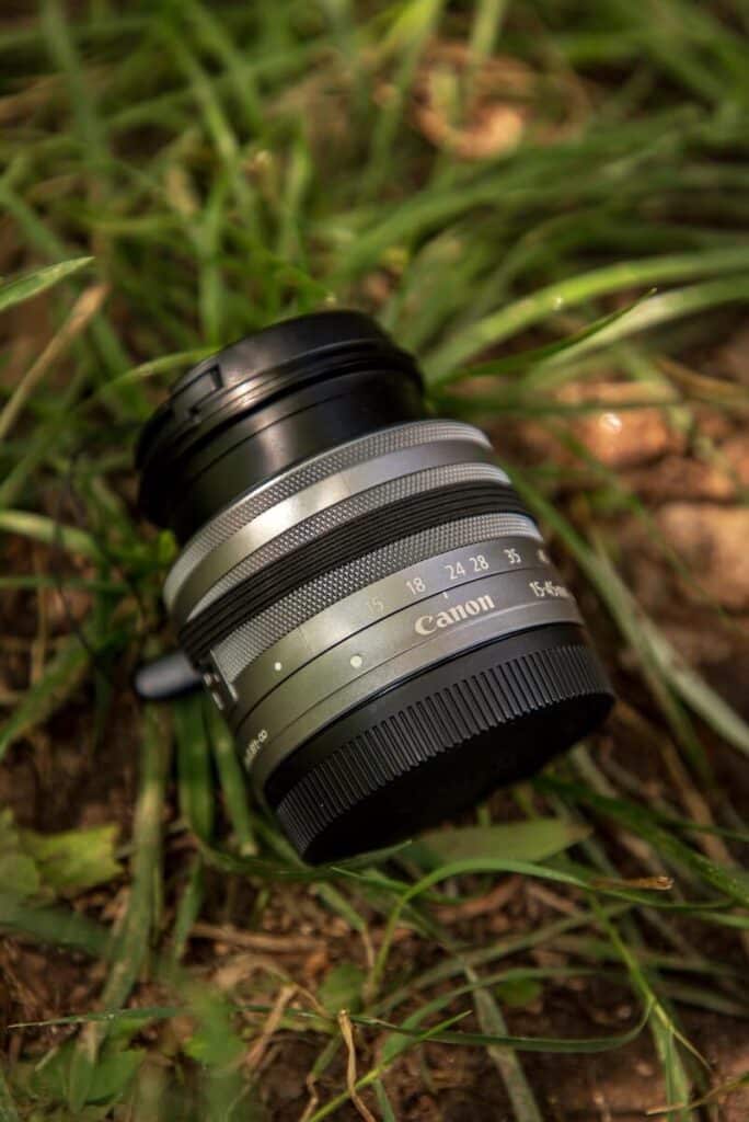 A 15-45mm lens sitting in the grass discussing the best lens for travel photography