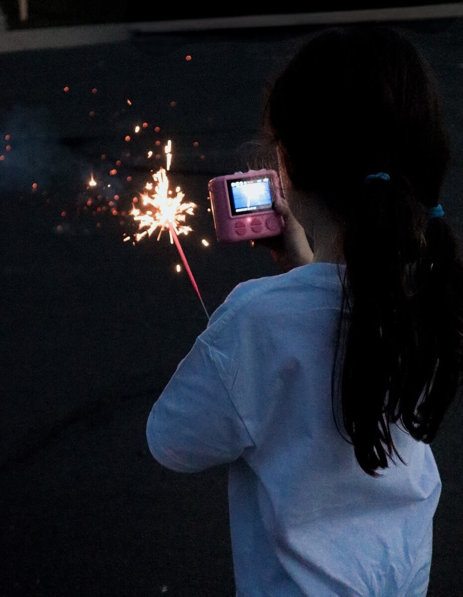A child taking a photo of a sparkler with a camera