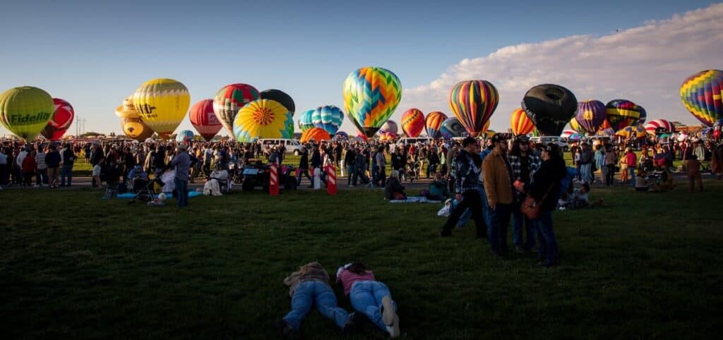 A panorama of balloons static on the ground and two girls laying down and a crowd at the International Balloon Fiesta in Albuquerque. 