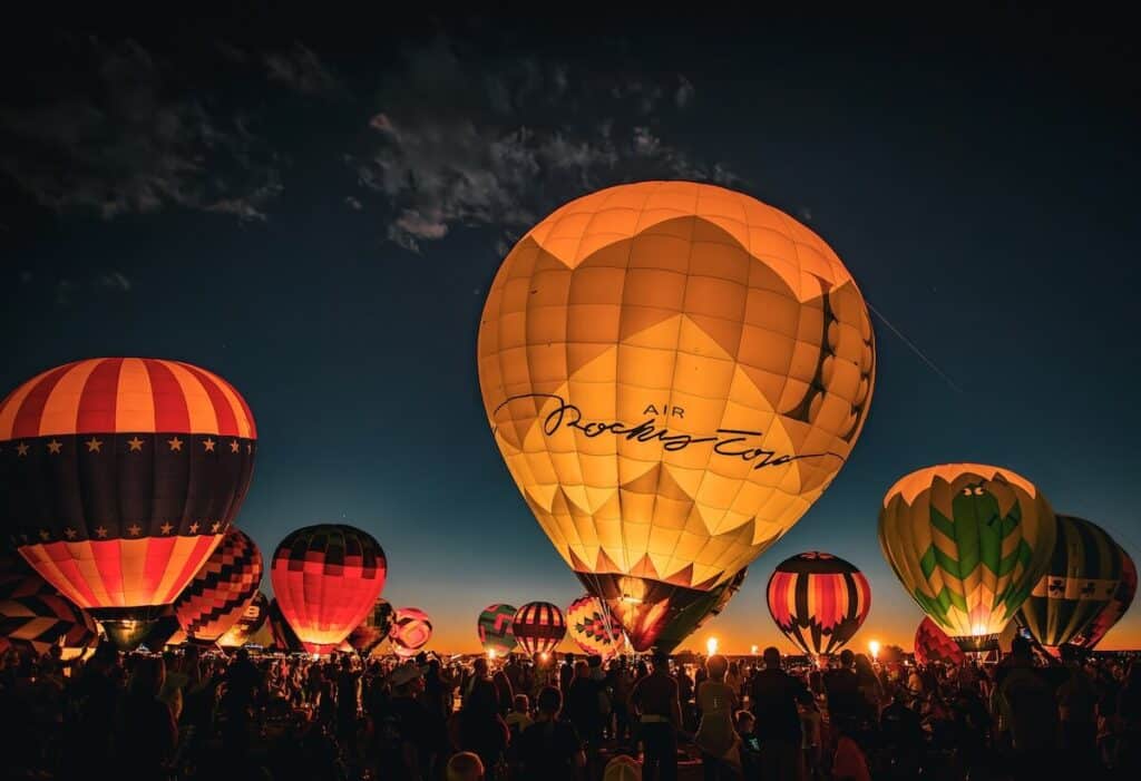 Several balloons in a line static on the ground "glowing" for the evening glow at the Albuquerque Balloon Fiesta 2025. 