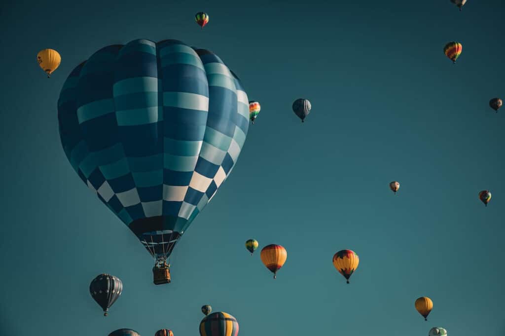 A blue photo of a single hot air balloon and in the distance is hundreds of smaller hot air balloons in New Mexico.