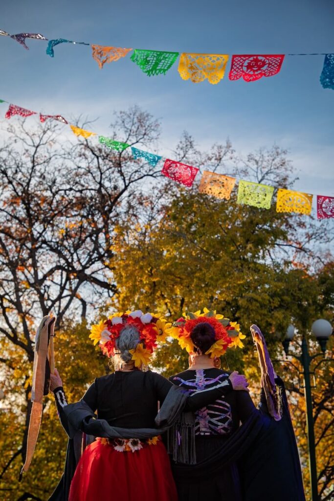 A grandmother and grandaughter posing with flags overhead in Sante Fe for Day of the Dead