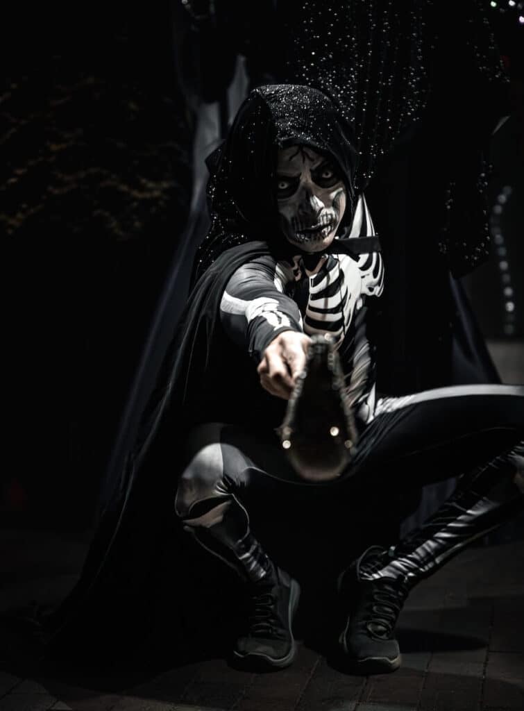 A man with skeleton facepaint and costume pointing a cane at the camera for a Dias De Los Meurtos Celebration