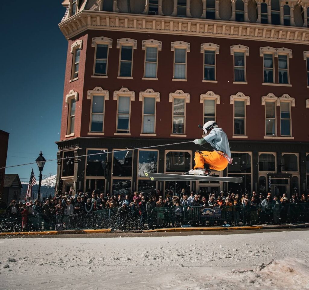 A skier in orange pants going off of a jump while being pulled by a horse in Colorado