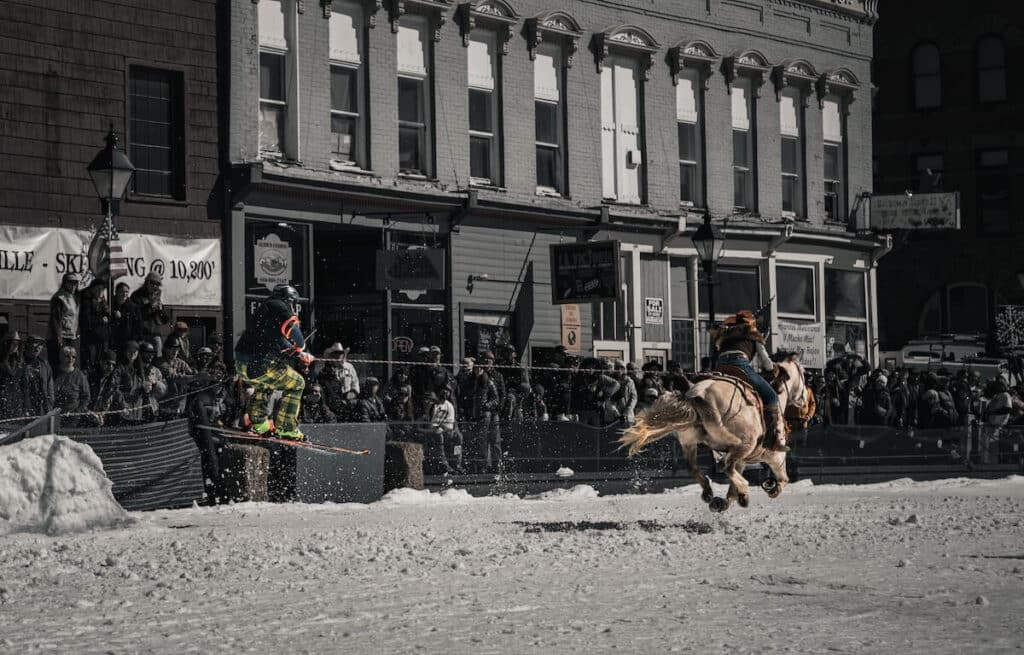 A black and white photo a horse pulling a skier for skijoring festivities in Colorado